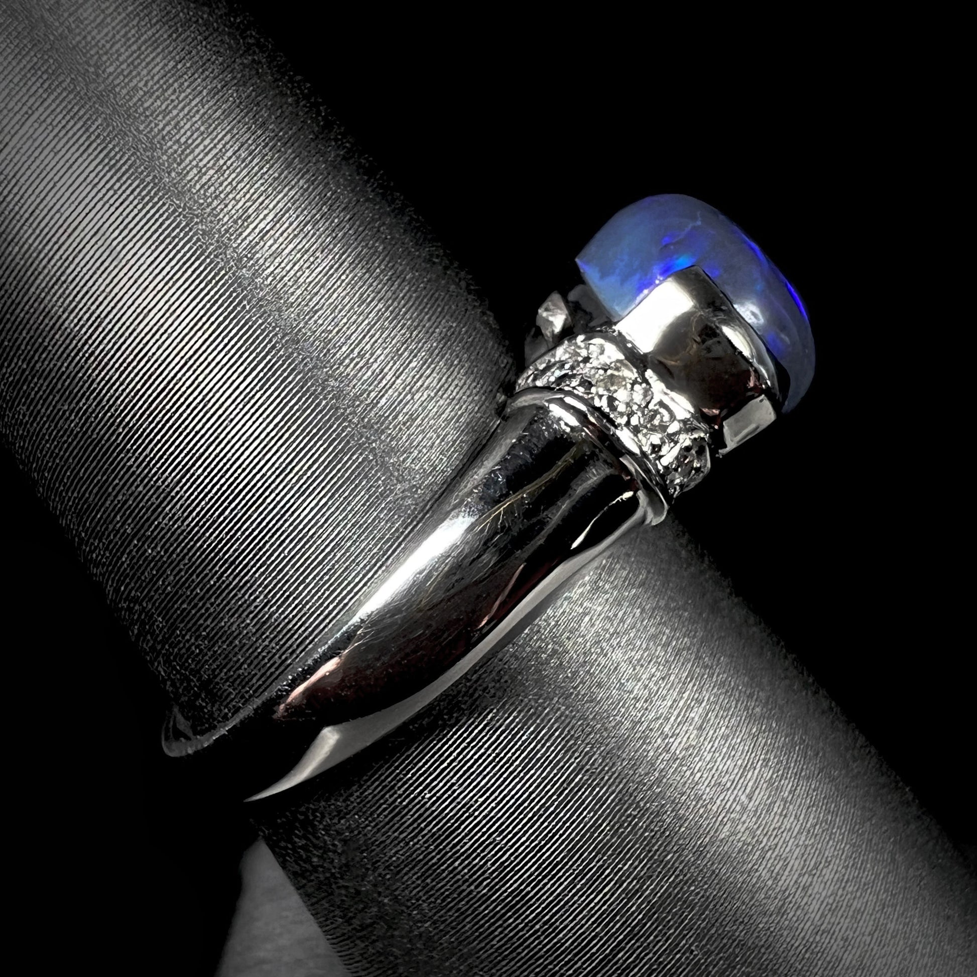 Side view of a platinum black opal and diamond ring.  The opal has blue color play.