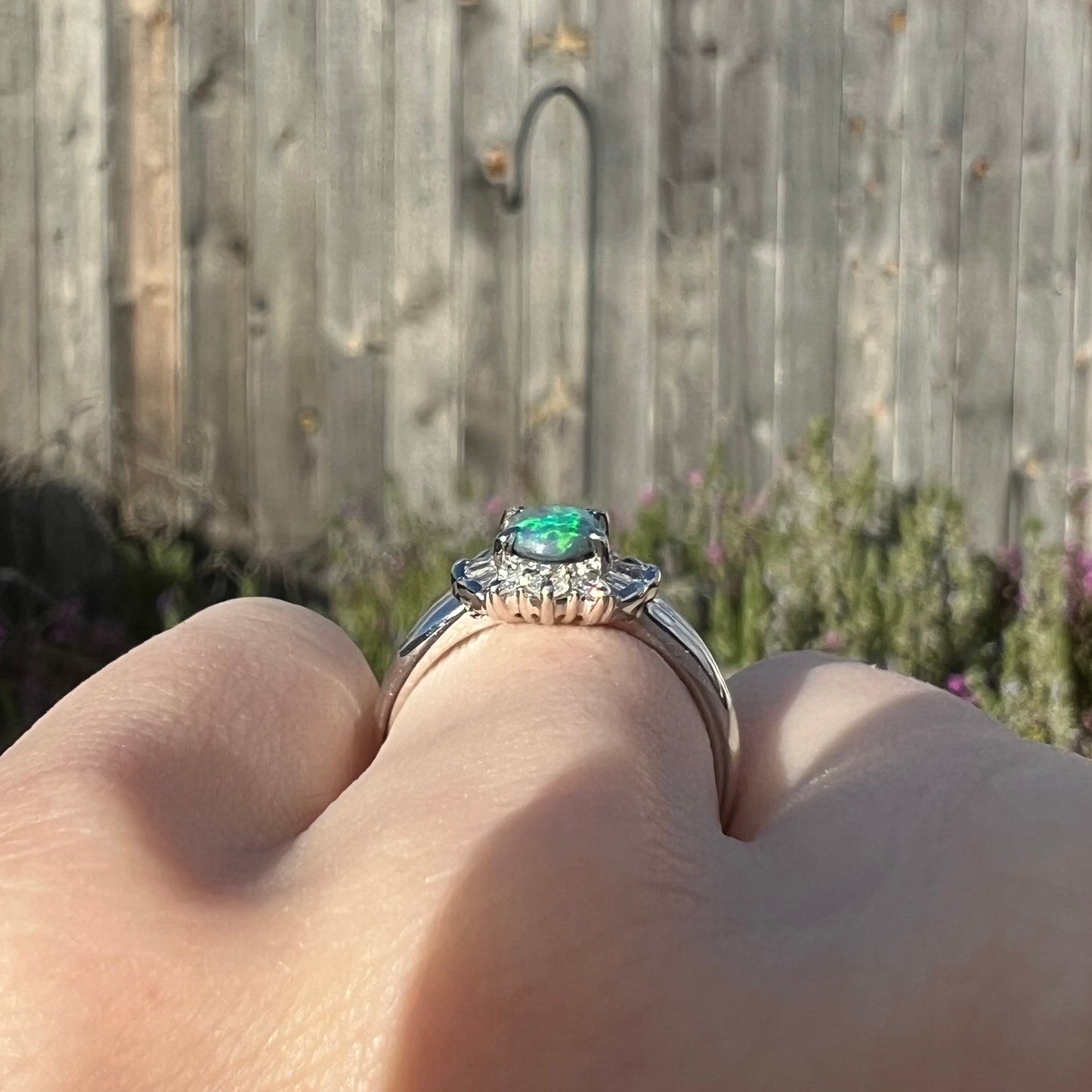 The gallery view of a platinum black opal engagement ring, worn on a hand in the sunlight.  The ring is low-profile.