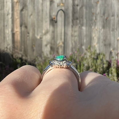 The gallery view of a platinum black opal engagement ring, worn on a hand in the sunlight.  The ring is low-profile.