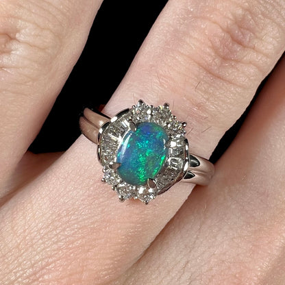 Macro closeup of hand wearing platinum black opal engagement ring showcasing blue color play in the opal.