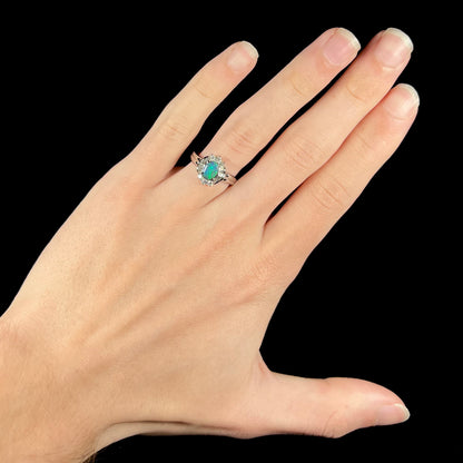 Hand wearing platinum black opal engagement ring on ring finger, held over a black background.