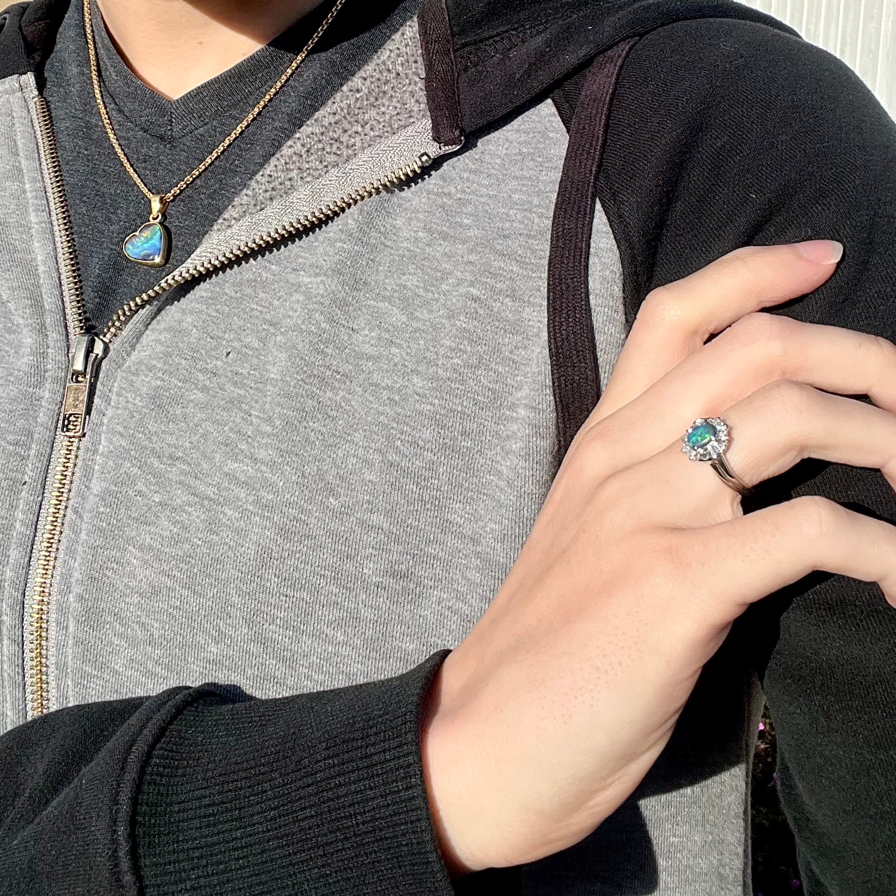 A platinum black opal engagement ring with a baguette diamond halo, demonstrated on a hand in the sunlight.