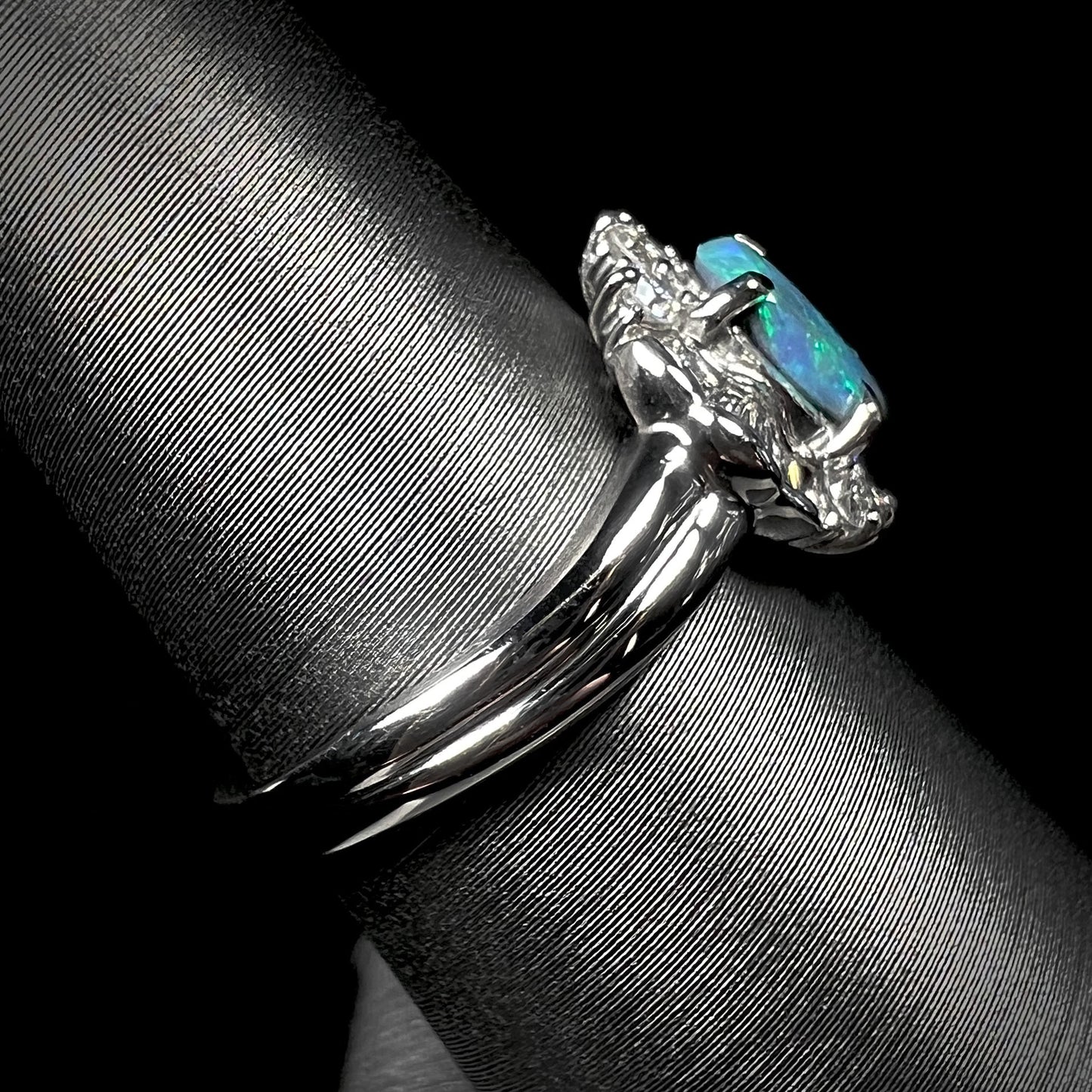 Side view of platinum black opal engagement ring showcasing the wavy shank and opal's dark body tone.