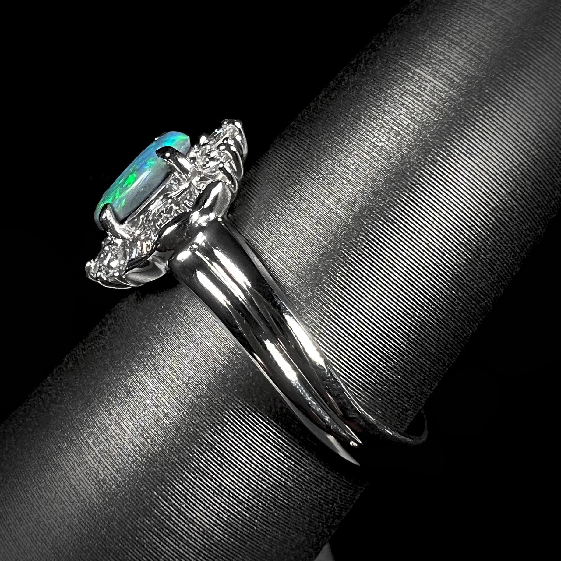 Side view of platinum black opal engagement ring, showcasing the wavy shank design and opal color play.