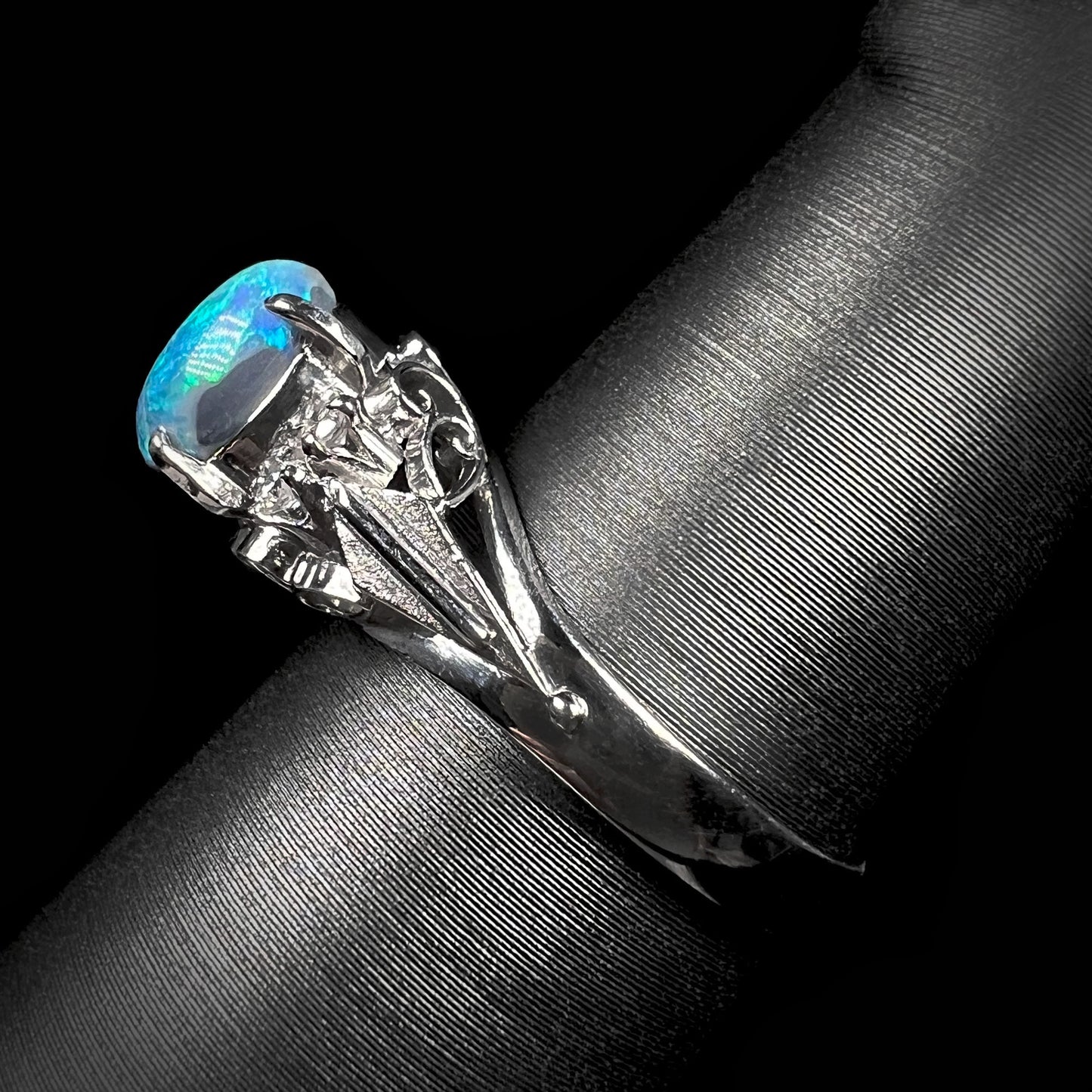 The side vew of a platinum black opal ring.  The ring's filigree design is partially visible.