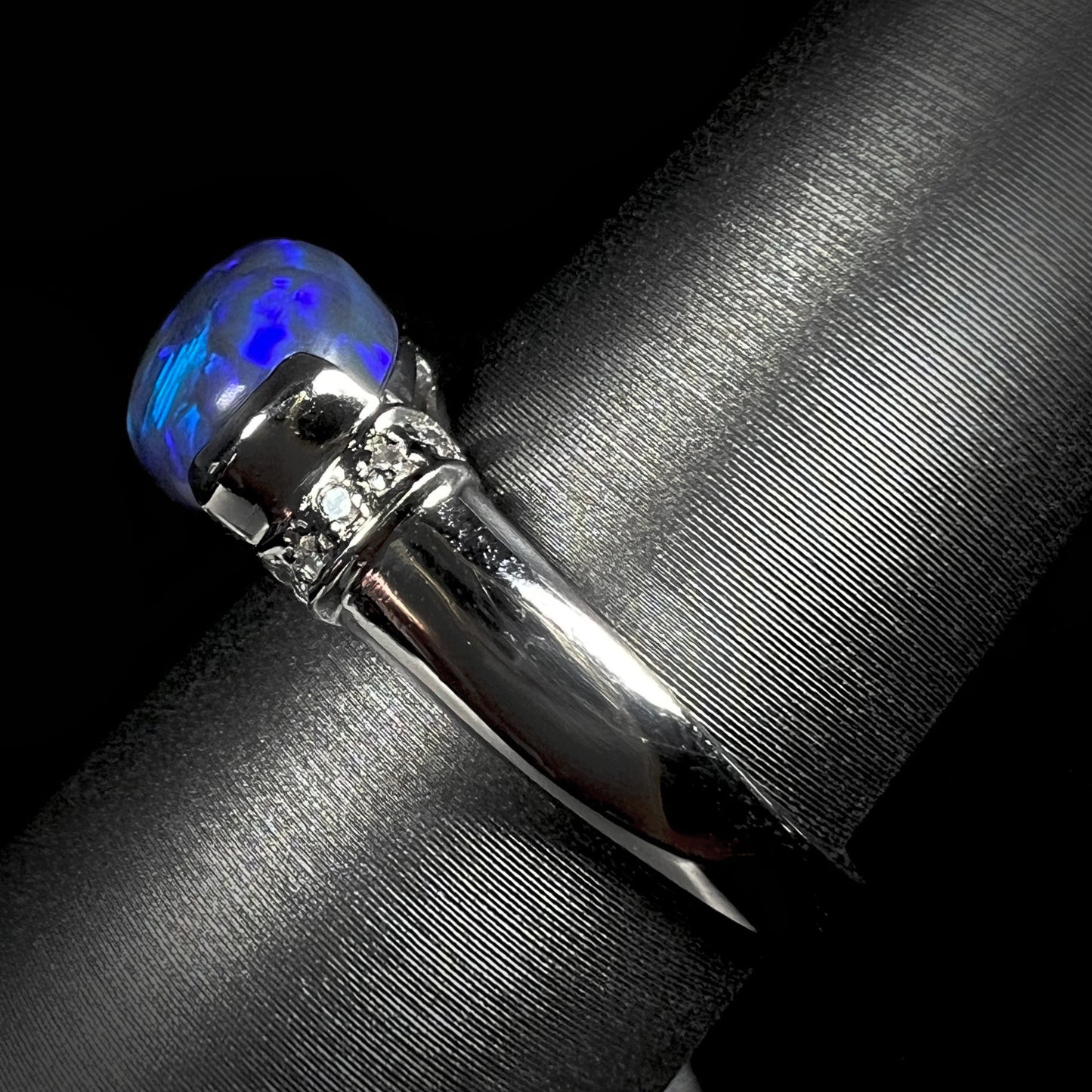 Side view of a platinum black opal ring with diamond accents.  The opal plays blue colors.