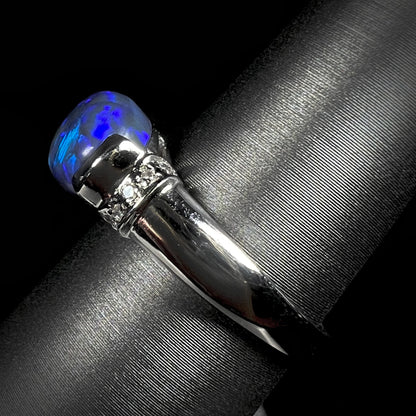 Side view of a platinum black opal ring with diamond accents.  The opal plays blue colors.