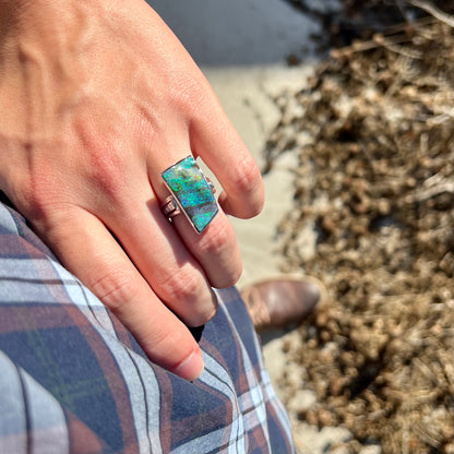 A platinum boulder opal and diamond ring with blue color play worn on a hand  as the hand rests on the model's hip.