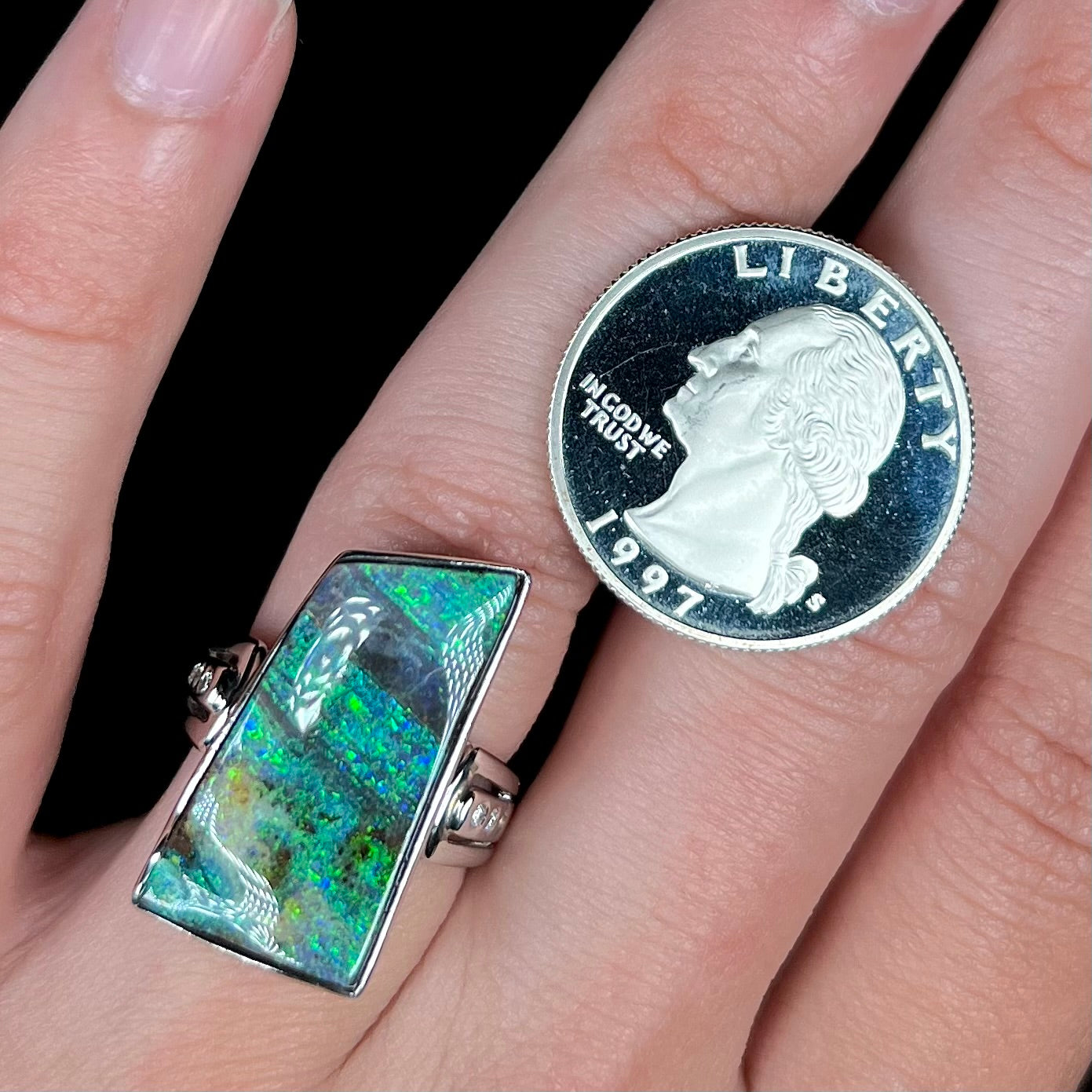 A platinum Australian boulder opal and diamond ring, worn on a hand next to a US quarter coin.