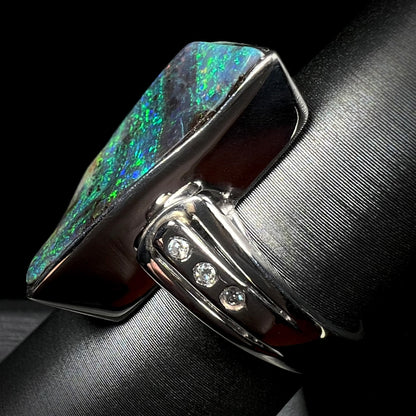 A platinum boulder opal ring with three visible diamond accents, shown from the side view on a ring display.