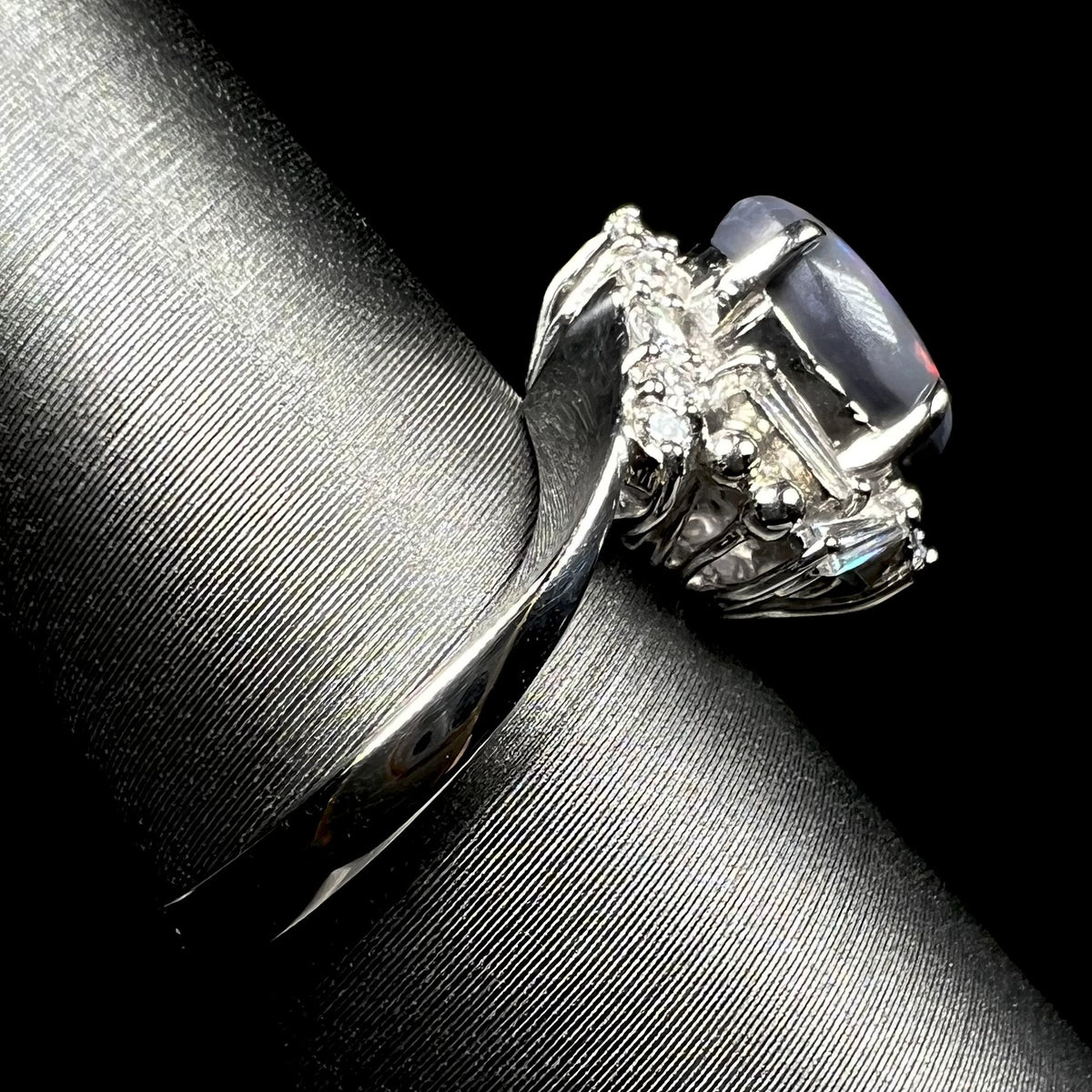 The side shank view of a platinum dark opal and diamond ring, shown on ring display.