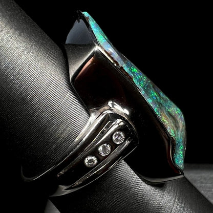 Side view of a platinum and diamond-accented boulder opal ring on a ring display.  Three diamonds are visible.