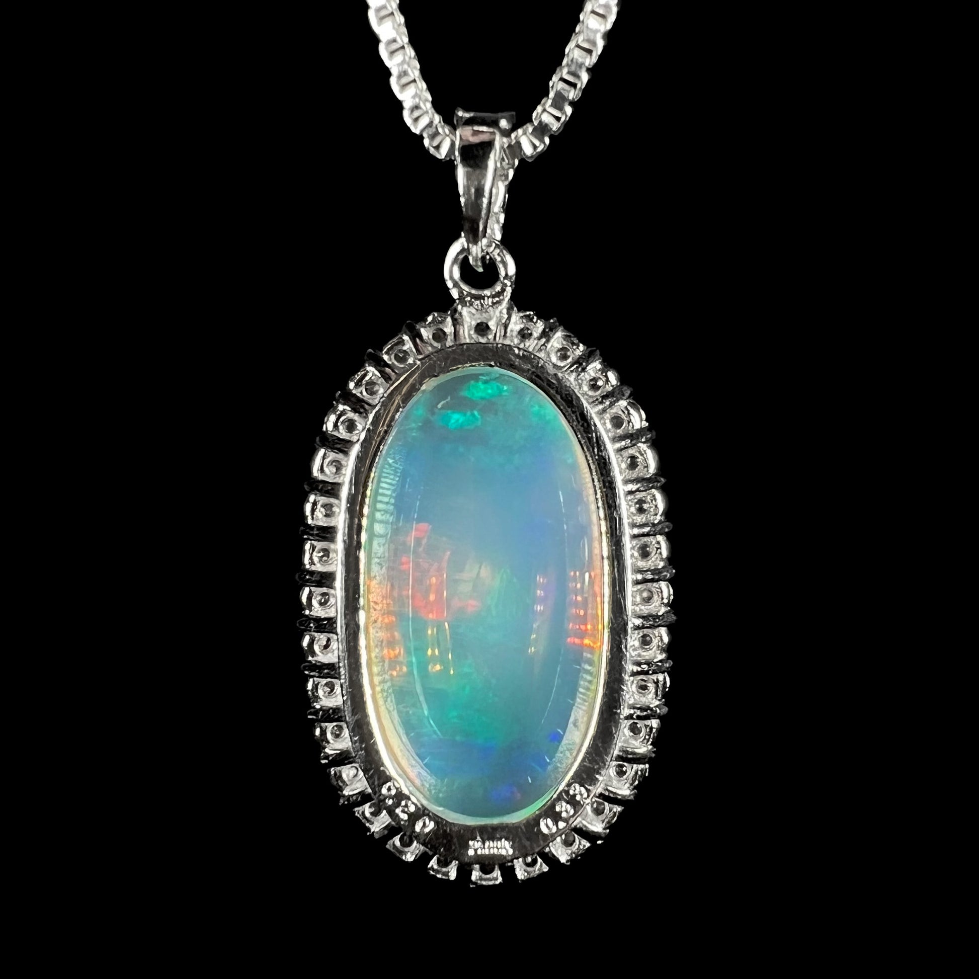 Back side of a platinum jelly opal pendant stamped "5.20", "Pt900", and "0.33", shown on a chain against a black background.