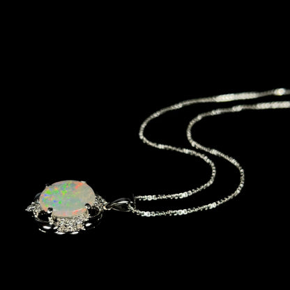 A platinum opal and diamond necklace, laying on a black backdrop, with the chain displayed in a wavy fashion.