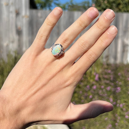 A platinum opal diamond ring on a hand in the natural sunlight.  The opal has green orange color play.