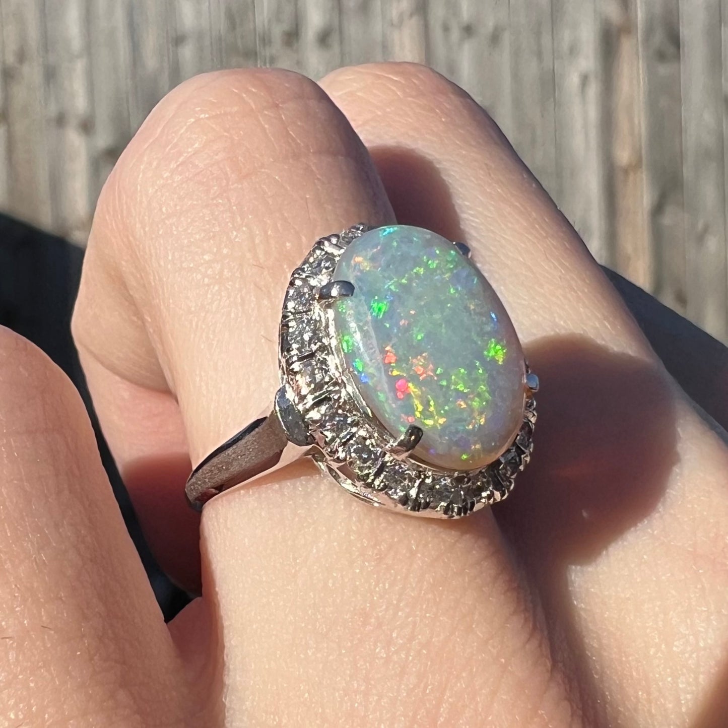 A vintage opal and diamond halo enggagement ring on a hand in the sunlight.