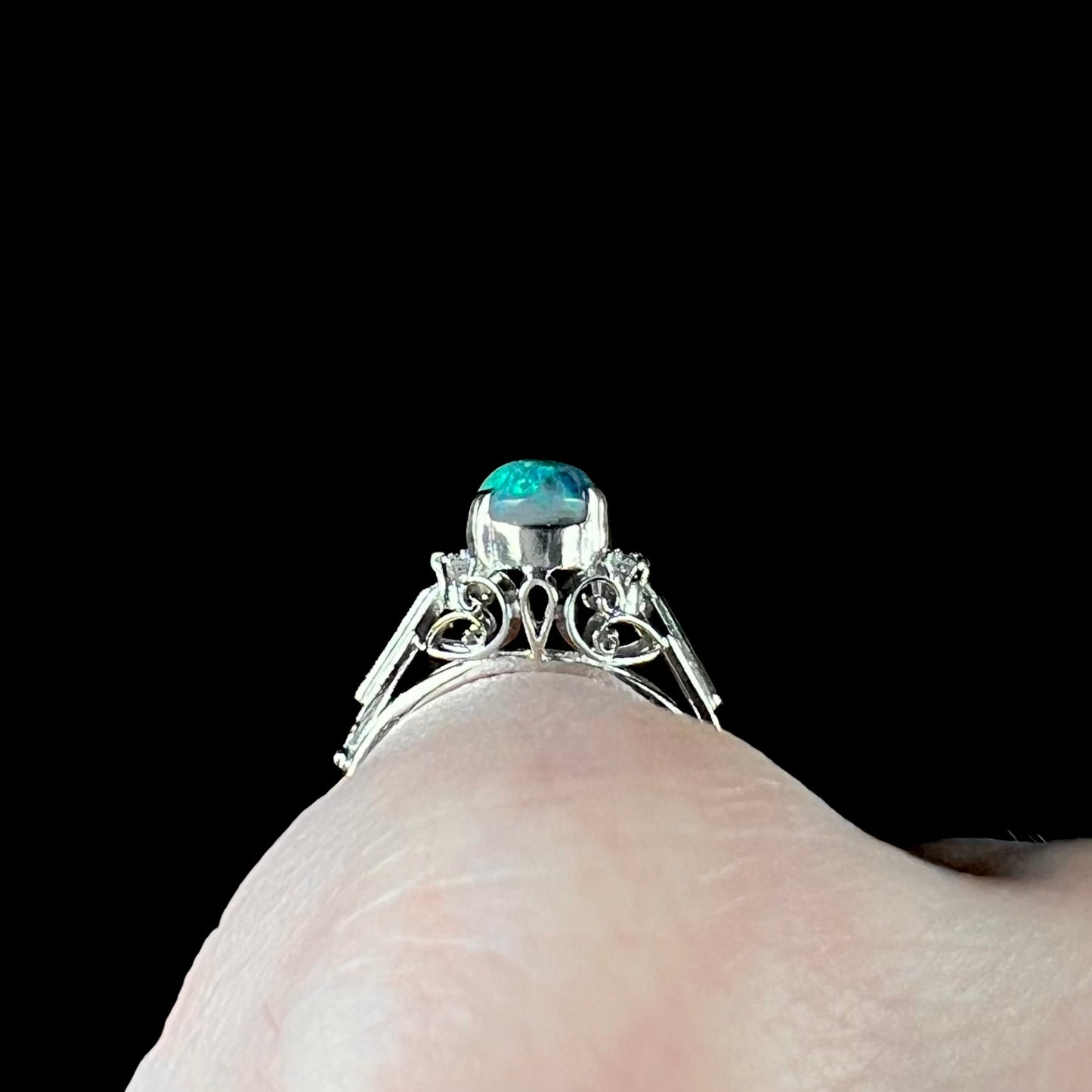 The gallery view of platinum filigree on a black opal ring while worn on a finger.