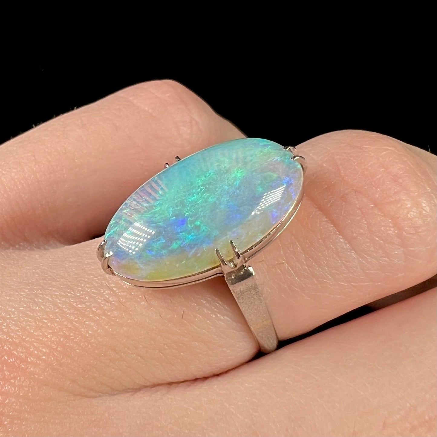 A platinum opal solitaire ring worn on a finger, showcasing its textured band.