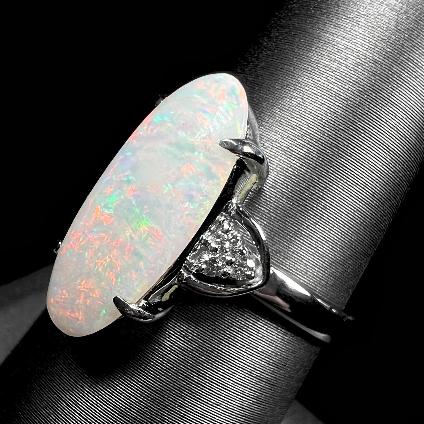 A Coober Pedy white opal platinum ring set with diamond accents.  The opal plays soft pink colors.