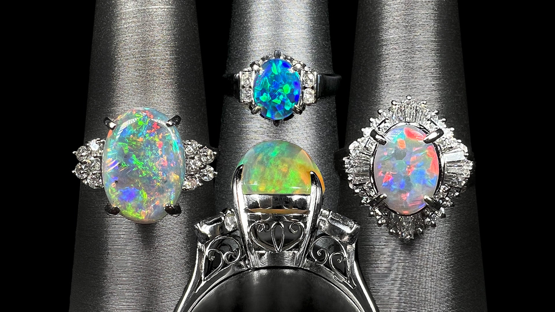 Four platinum opal and diamond rings.  Three are facing the camera, one is seen from a side profile gallery angle showing its delicate open filigree design.