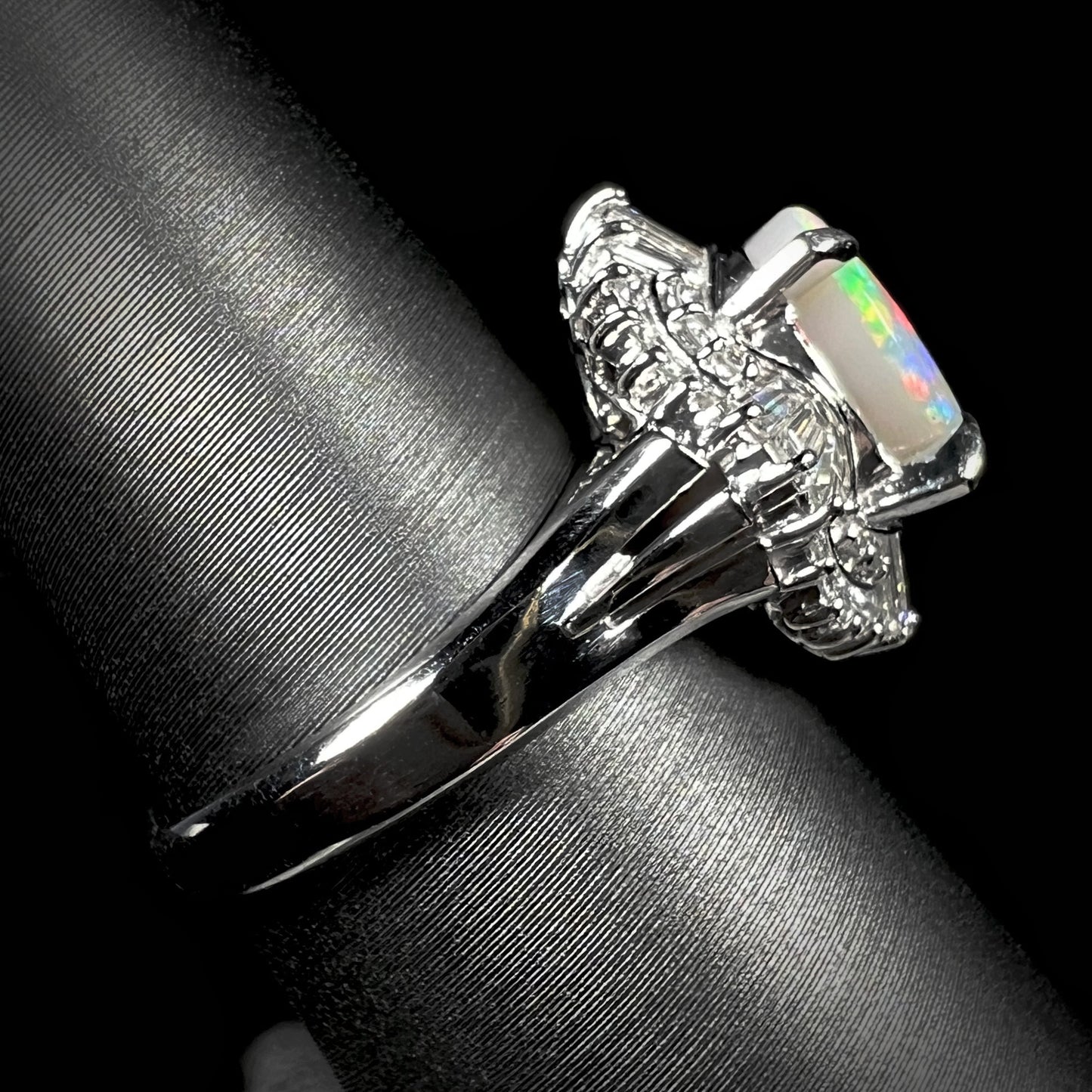 Side view of a platinum semi-black opal and diamond ring, showcasing its vintage filigree undercarriage and diamond spray setting.