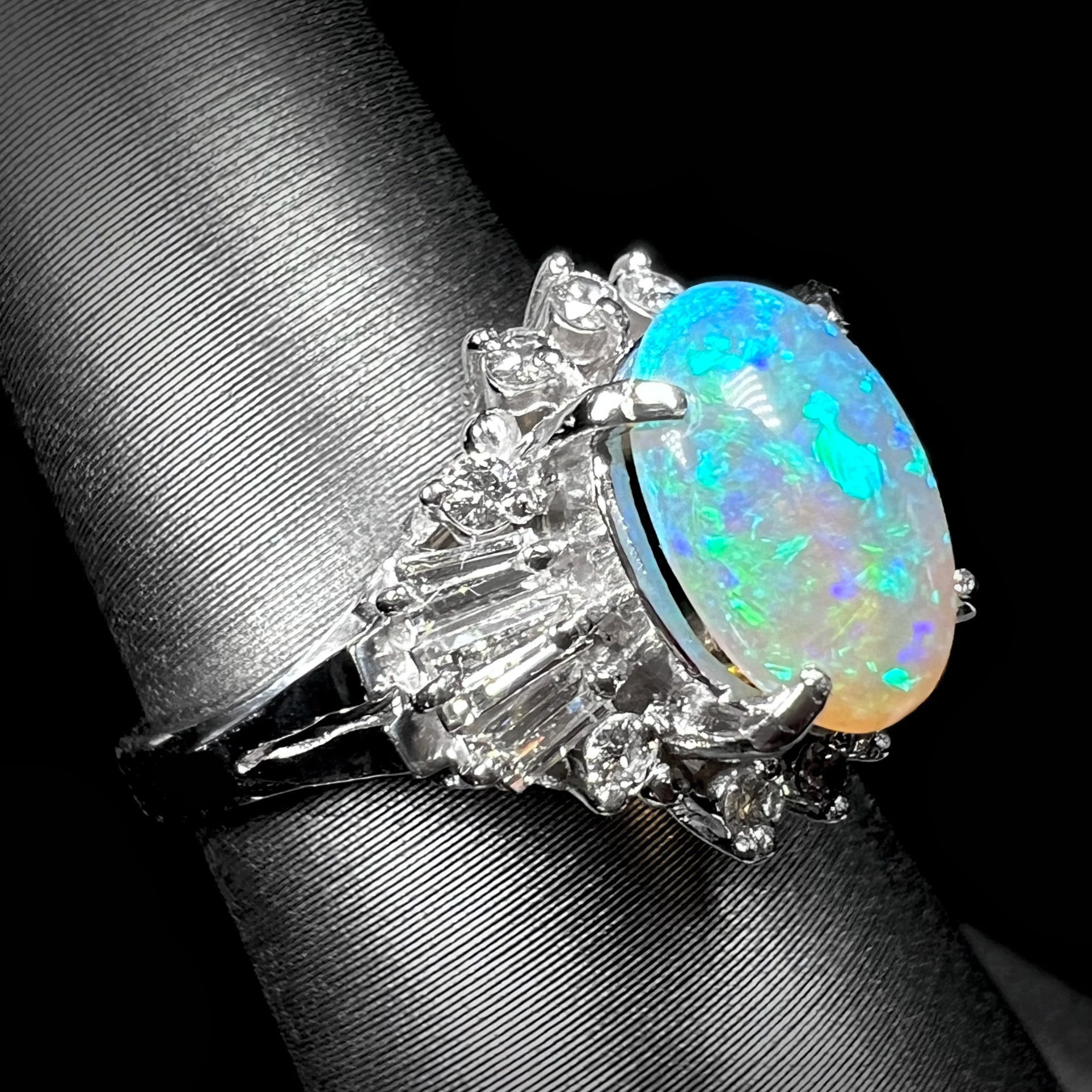 Rotated view of platinum semi-crystal opal engagement ring showing diamond baguettes and blue color play in the opal.