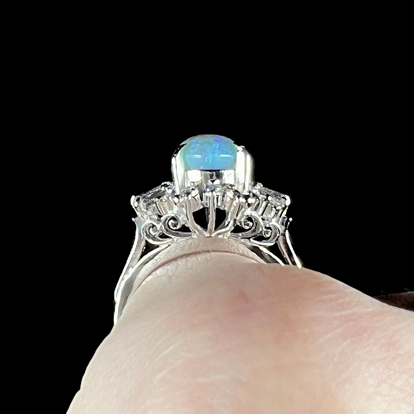 Gallery filigree view of platinum semi-crystal opal engagement ring worn on finger against black background.