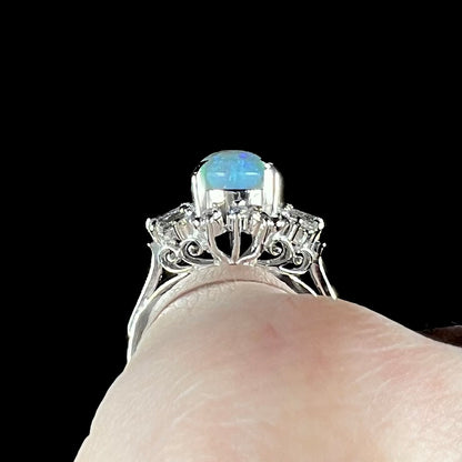 Gallery filigree view of platinum semi-crystal opal engagement ring worn on finger against black background.