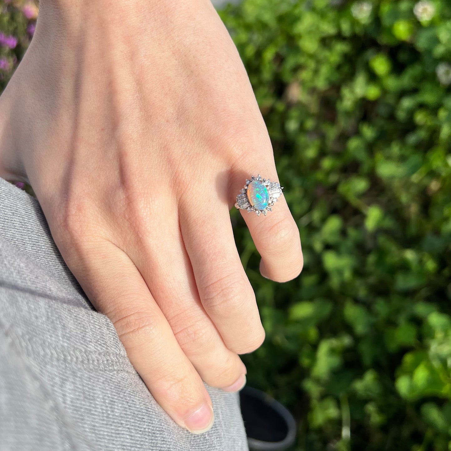 Hand on hip wearing platinum semi-crystal opal engagement ring on pinkie in sunlight.