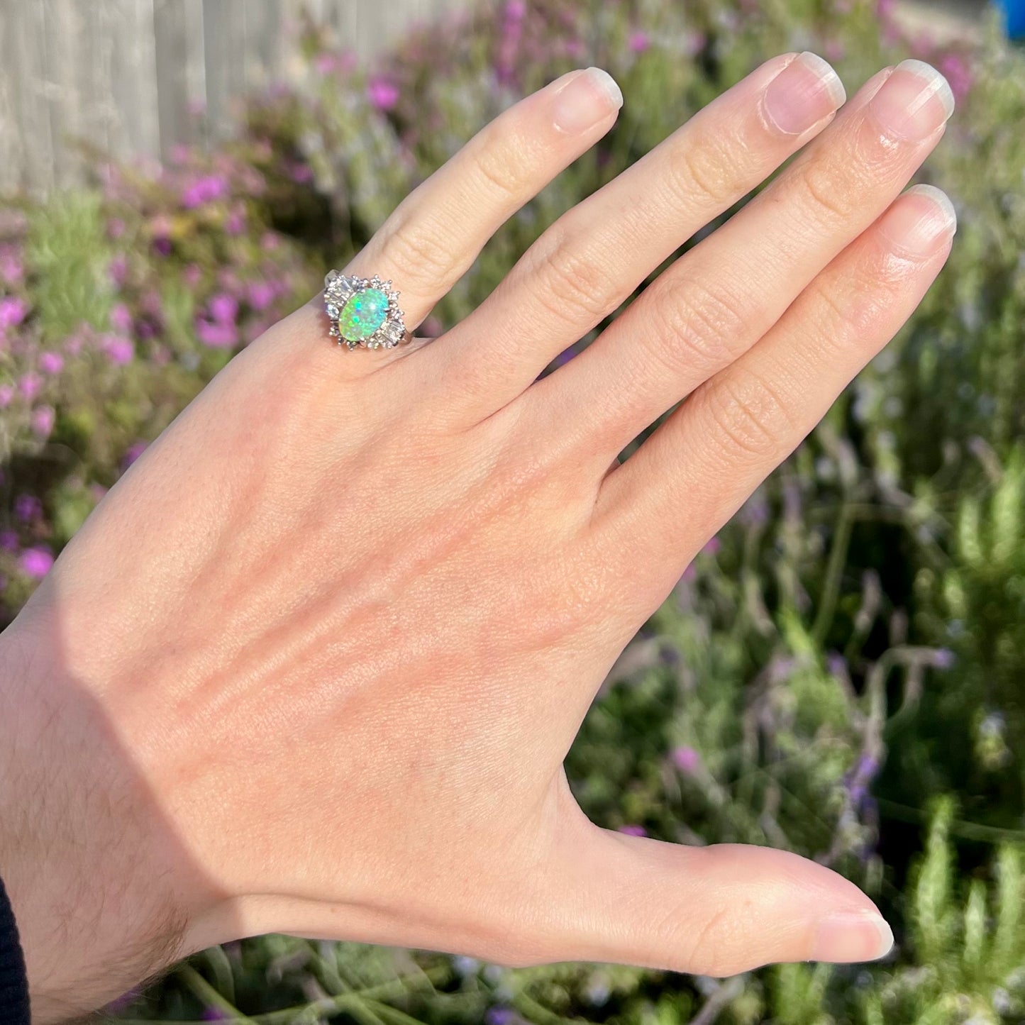 Platinum semi-crystal opal engagement ring worn on pinkie outside in sunlight, showcasing green opal color play.