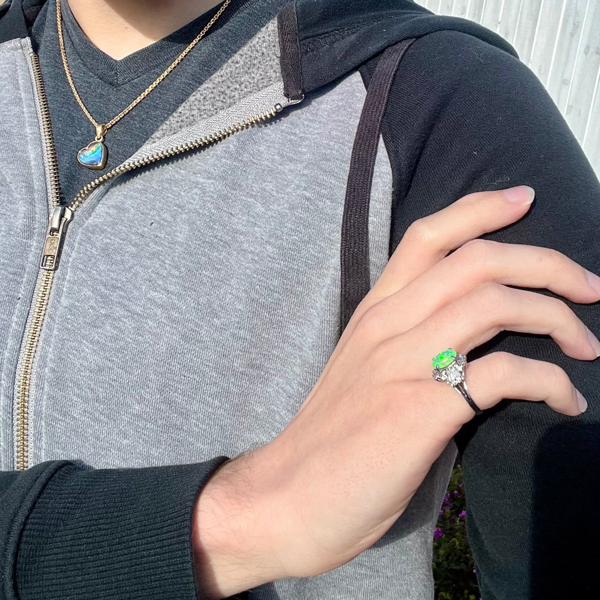 Platinum semi-crystal opal engagement ring worn on model's hand, crossing torso and resting on opposite shoulder, with vivid bright green color play.