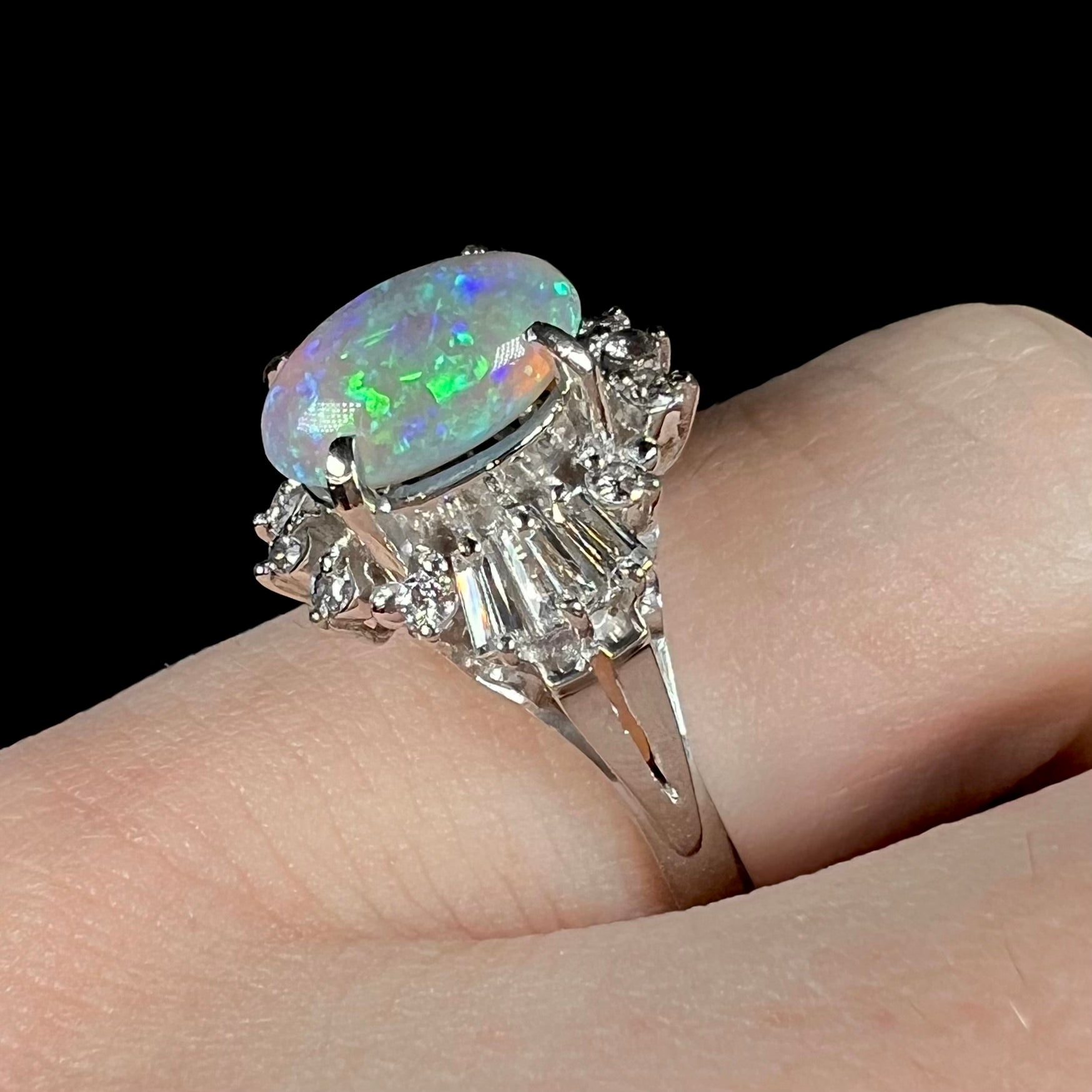 Diagonal angled view of platinum semi-crystal opal engagement ring worn on pinkie finger, showcasing baguette diamonds and green opal color play.