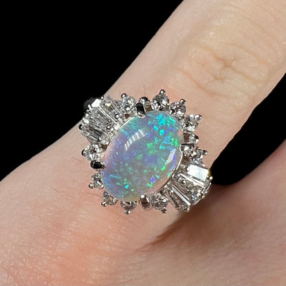 Macro closeup of platinum semi-crystal opal engagement ring worn on pinkie, showcasing blue color play in the opal.