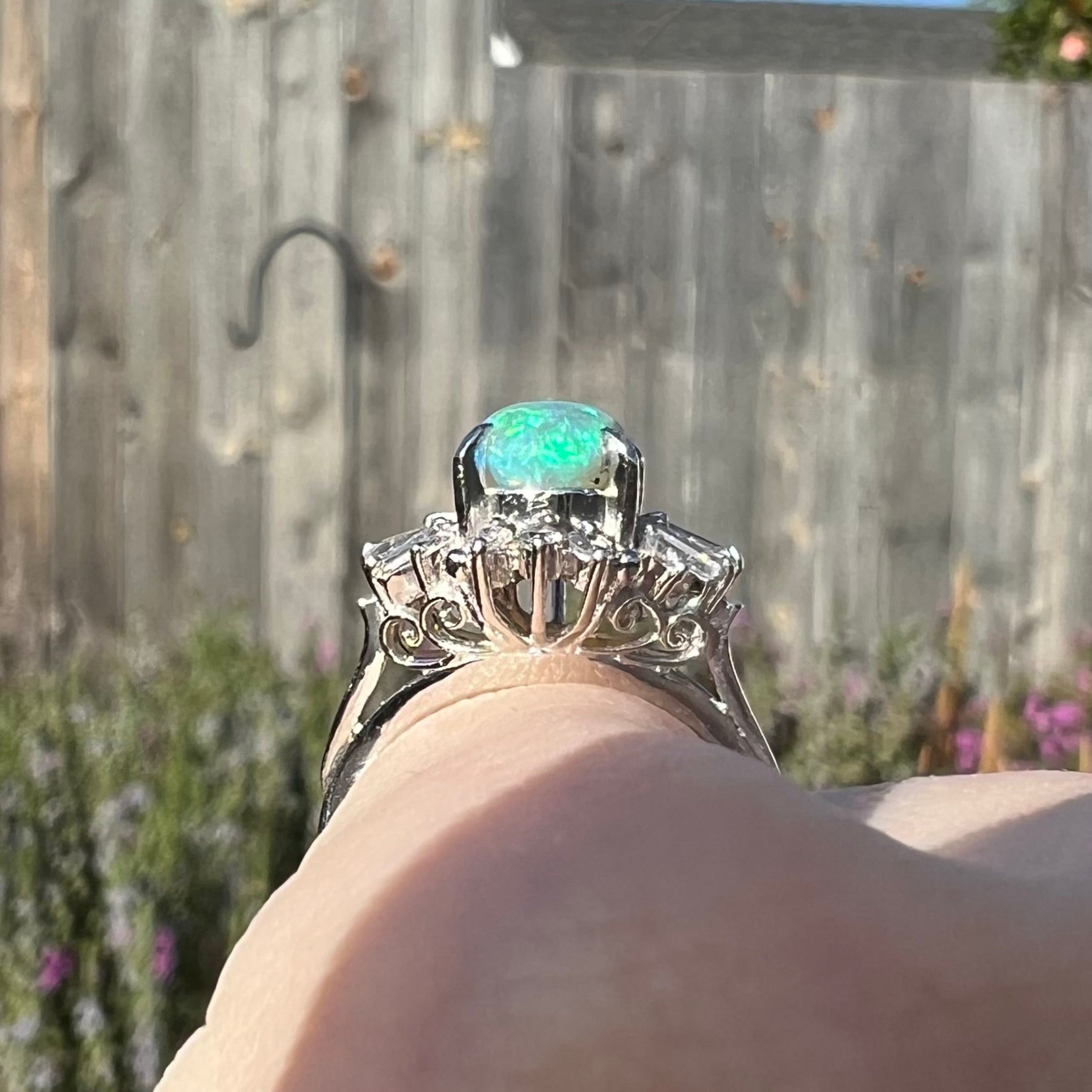 Gallery view of platinum semi-crystal opal engagement ring on pinkie worn outside, showcasing filigree details.