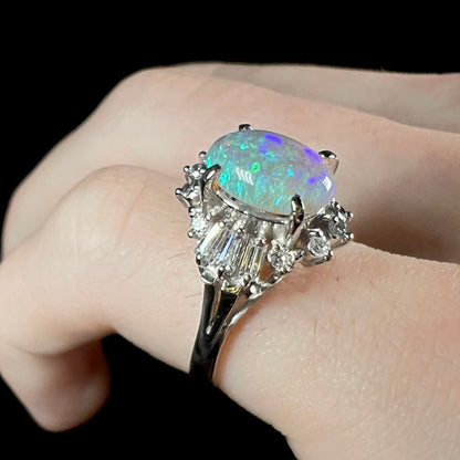 Opposite angled view of platinum semi-crystal opal engagement ring worn on pinkie, showcasing blue color play.