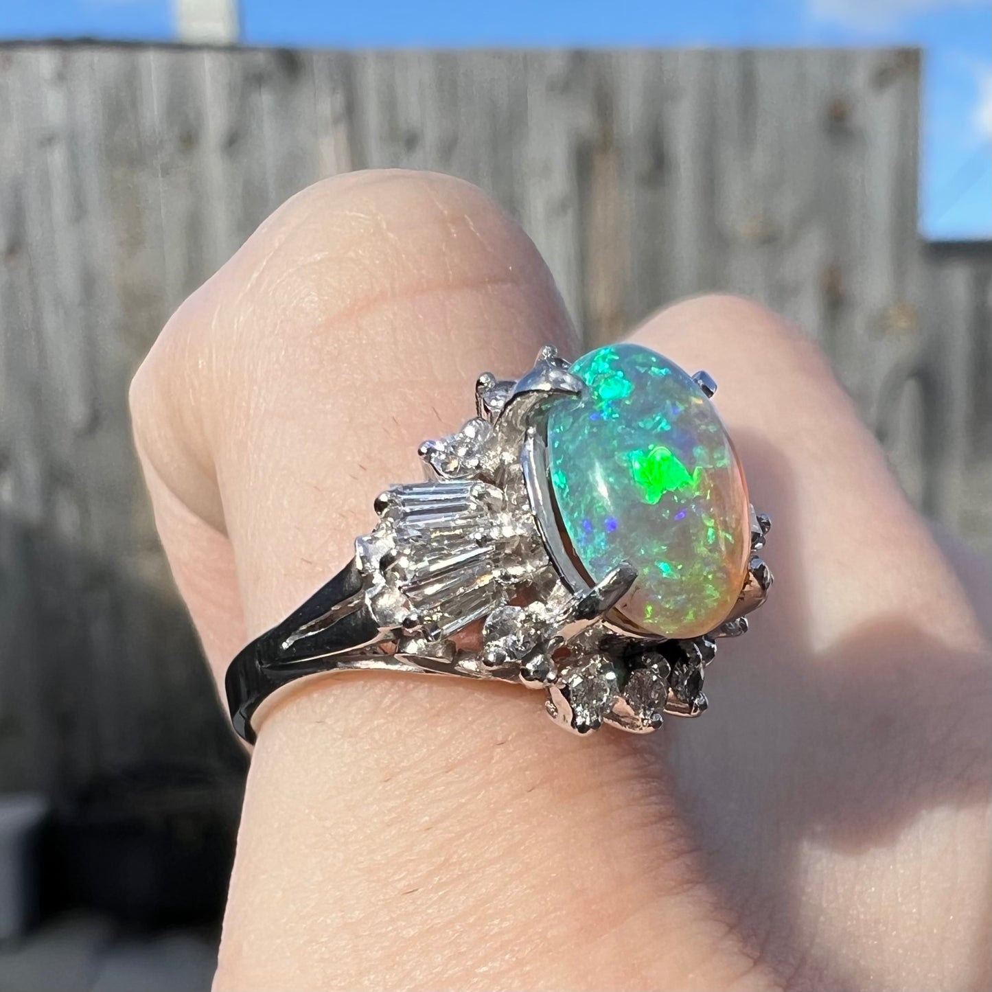 Opposite side view of platinum semi-crystal opal engagement ring on pinkie finger, showcasing green opal color play.