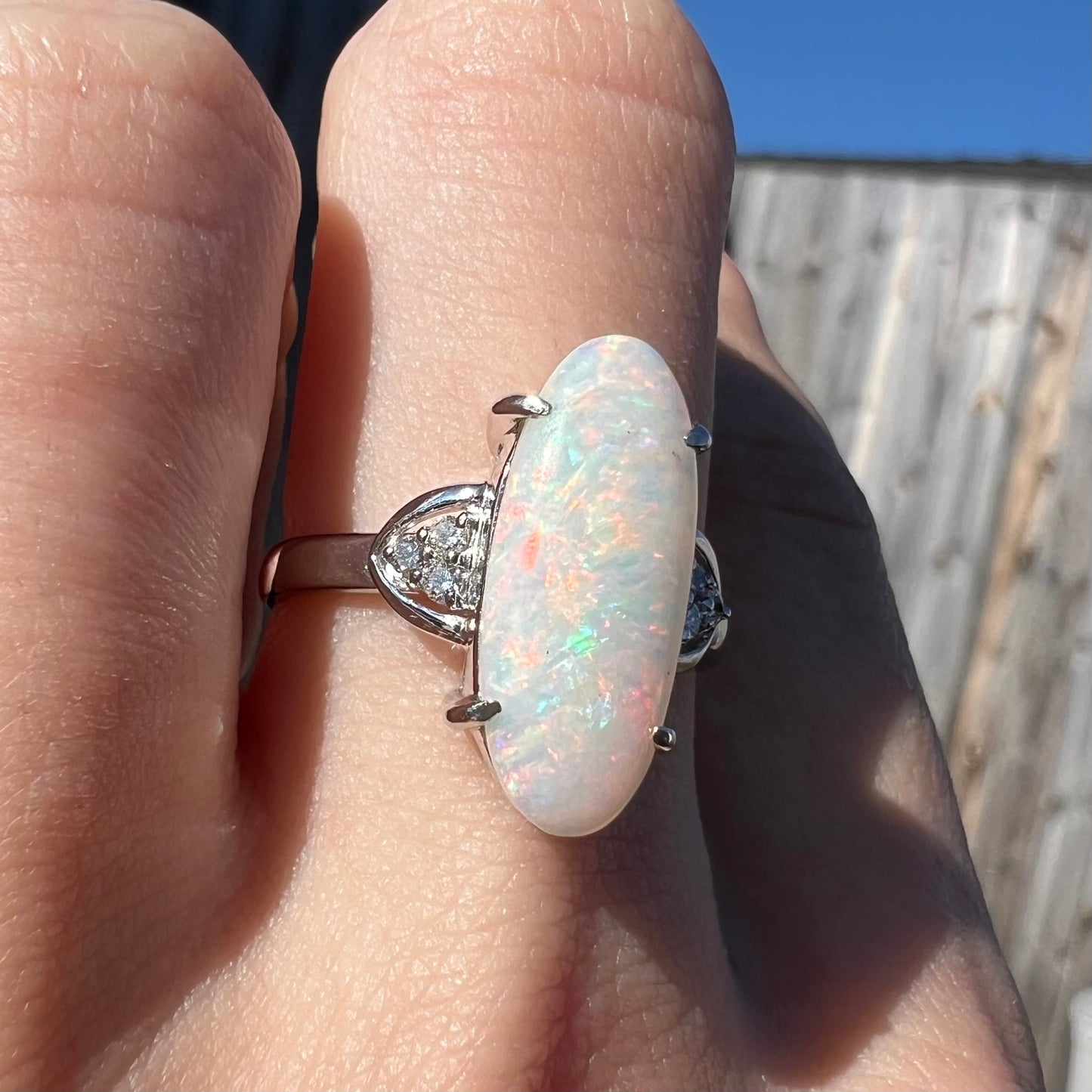 A Coober Pedy white opal platinum ring set with diamond accents.  The opal plays soft pink colors.