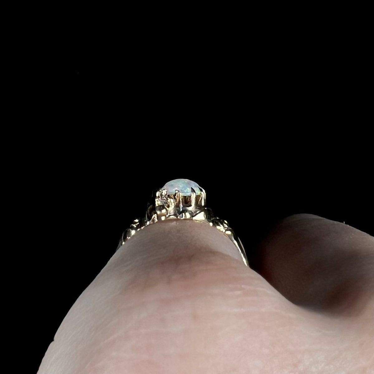 Side profile gallery view of a gold Art Nouveau opal pinky ring, worn on hand; the ring's prongs are primarily in view