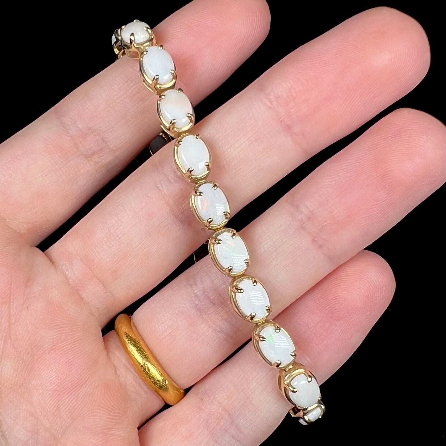 Hand holding 10k yellow gold prong-set white opal tennis bracelet.