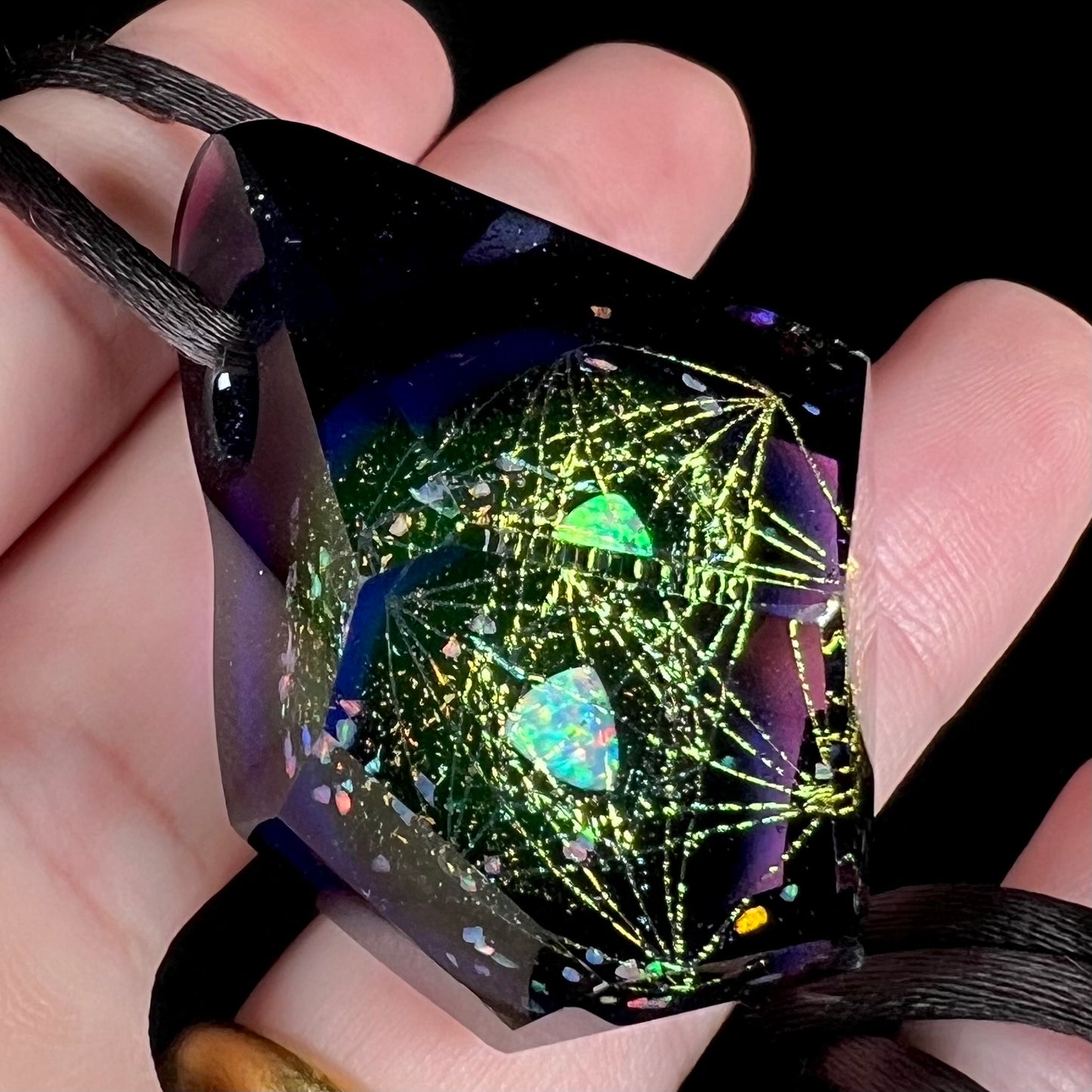 Angled close-up of a purple glass and trillion cut lab opal pendant, held in a hand.