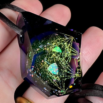 Angled close-up of a purple glass and trillion cut lab opal pendant, held in a hand.