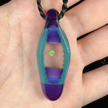 A purple and teal borosilicate glass and lab-created opal pendant shown close-up, held in a hand.