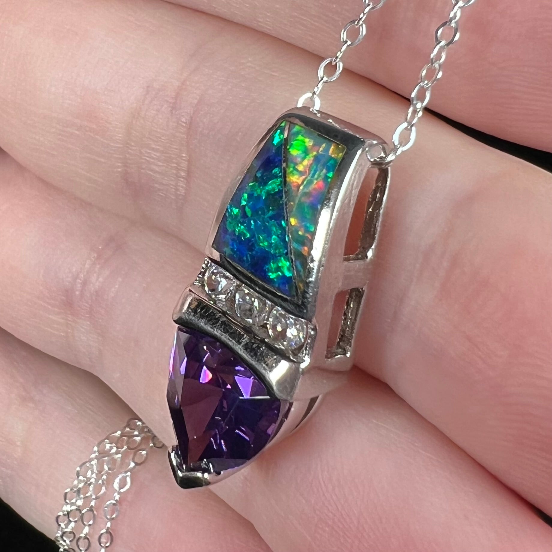 An estate sterling silver drop pendant set with lab-created opal inlay and a purple trillion cut CZ stone, shown close-up from an angle resting on fingers.