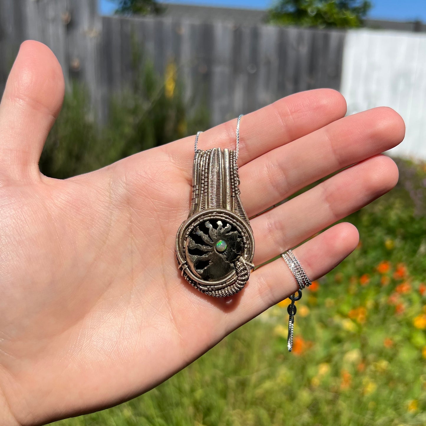 Man's wire-wrapped pyritized ammonite fossil pendant with Ethiopian opal accent held in hand in natural sunlight.