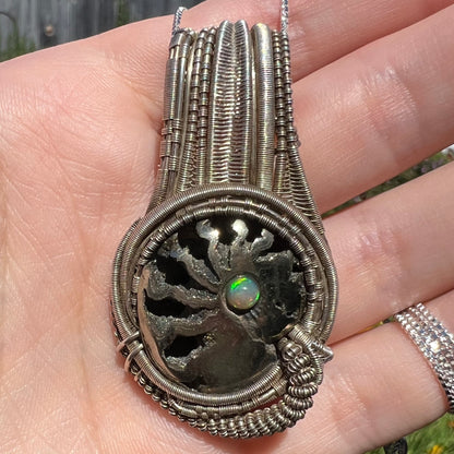 Close-up macro view of pyritized ammonite pendant with silver wire wrap design and opal accent, shown from front in natural light.