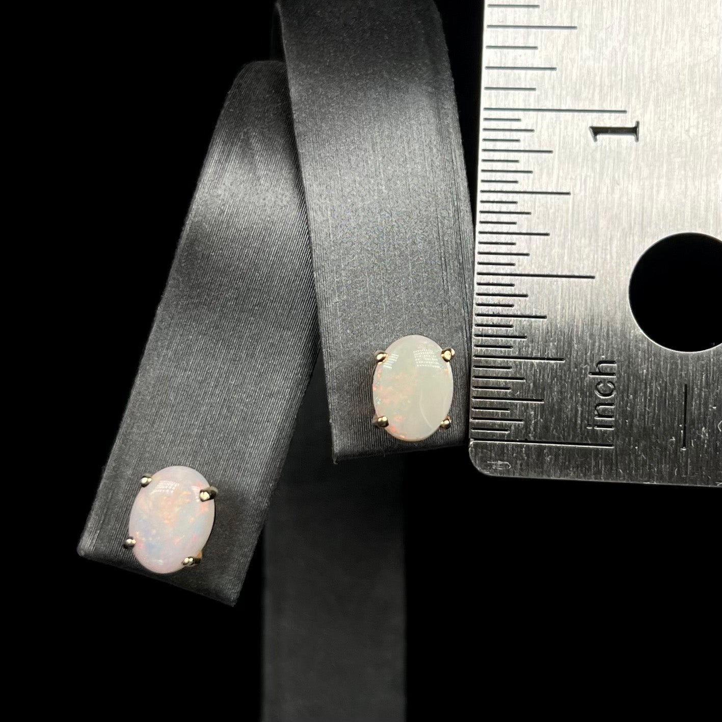 Quarter of an inch long opal stud earrings on display next to ruler