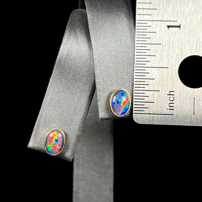 Pair of opal triplet stud earrings in gold that measure one-quarter of an inch long, shown on earring display next to ruler