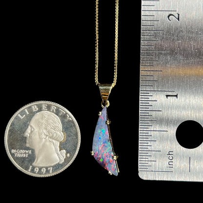 Freeform shaped boulder opal pendant in 18k gold next to ruler and quarter coin, measuring 1.25 inches long