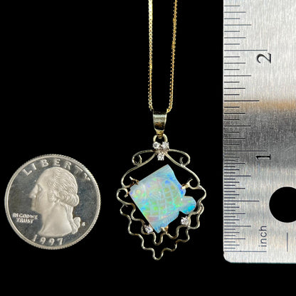 1.5 inch-long quarter-sized Australian opal and diamond fish pendant in gold shown between US quarter coin and ruler