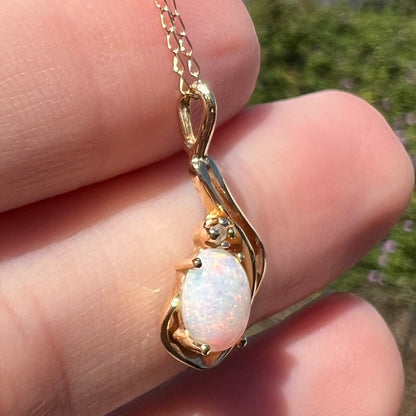 Angled close-up of real Australian opal pendant in 14k gold with diamond accent, held in natural light